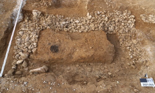 Unter dem Kellerboden der alten «Rheinlust» kamen noch weitere Fundamentreste eines Grabmonuments zum Vorschein (Gerölle). Beim dunklen Fleck in der linken Bildhälfte handelt es sich um eine Brandbestattung in einer Keramik-Urne. © Augusta Raurica